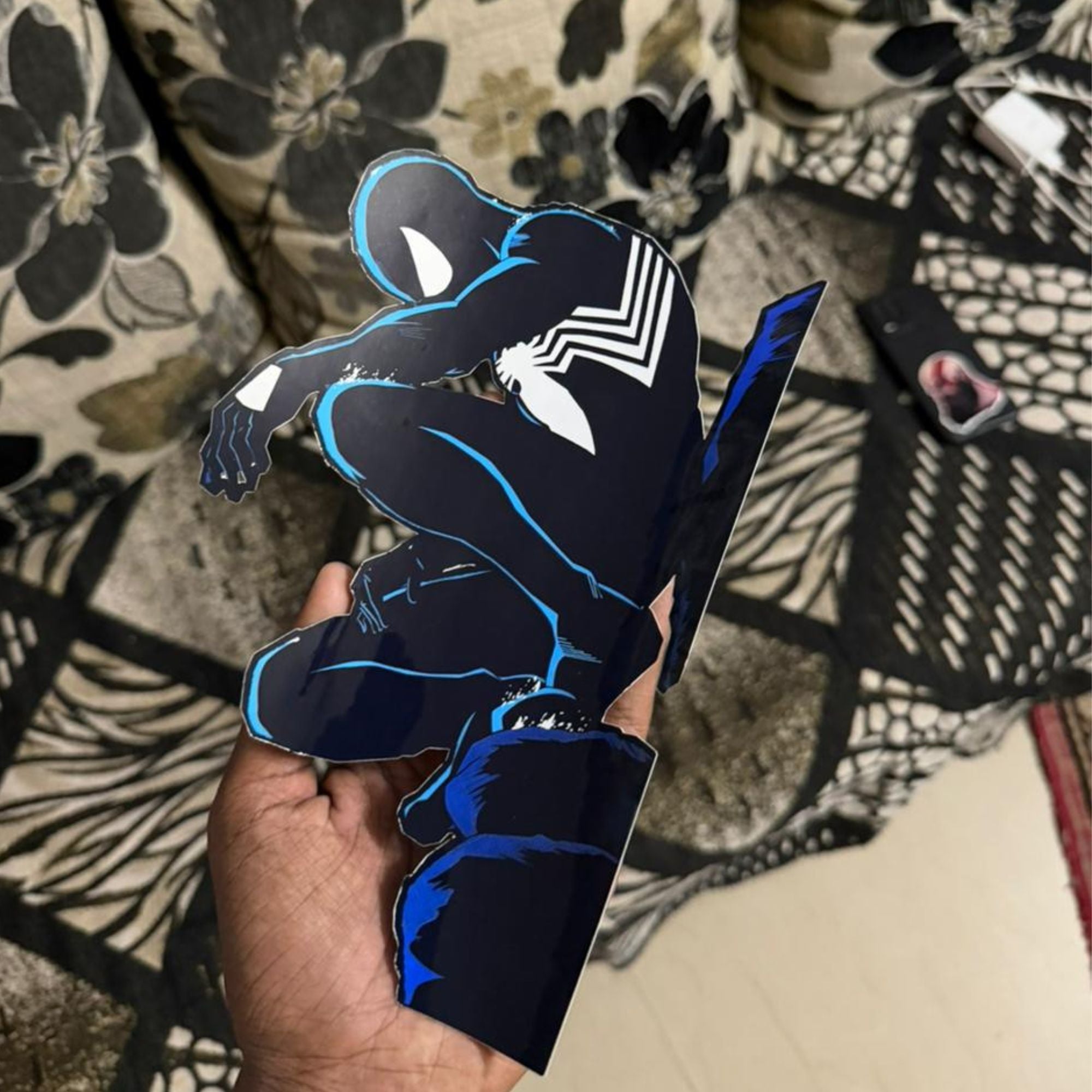 Hand holding a black and blue superhero cutout against a patterned fabric background