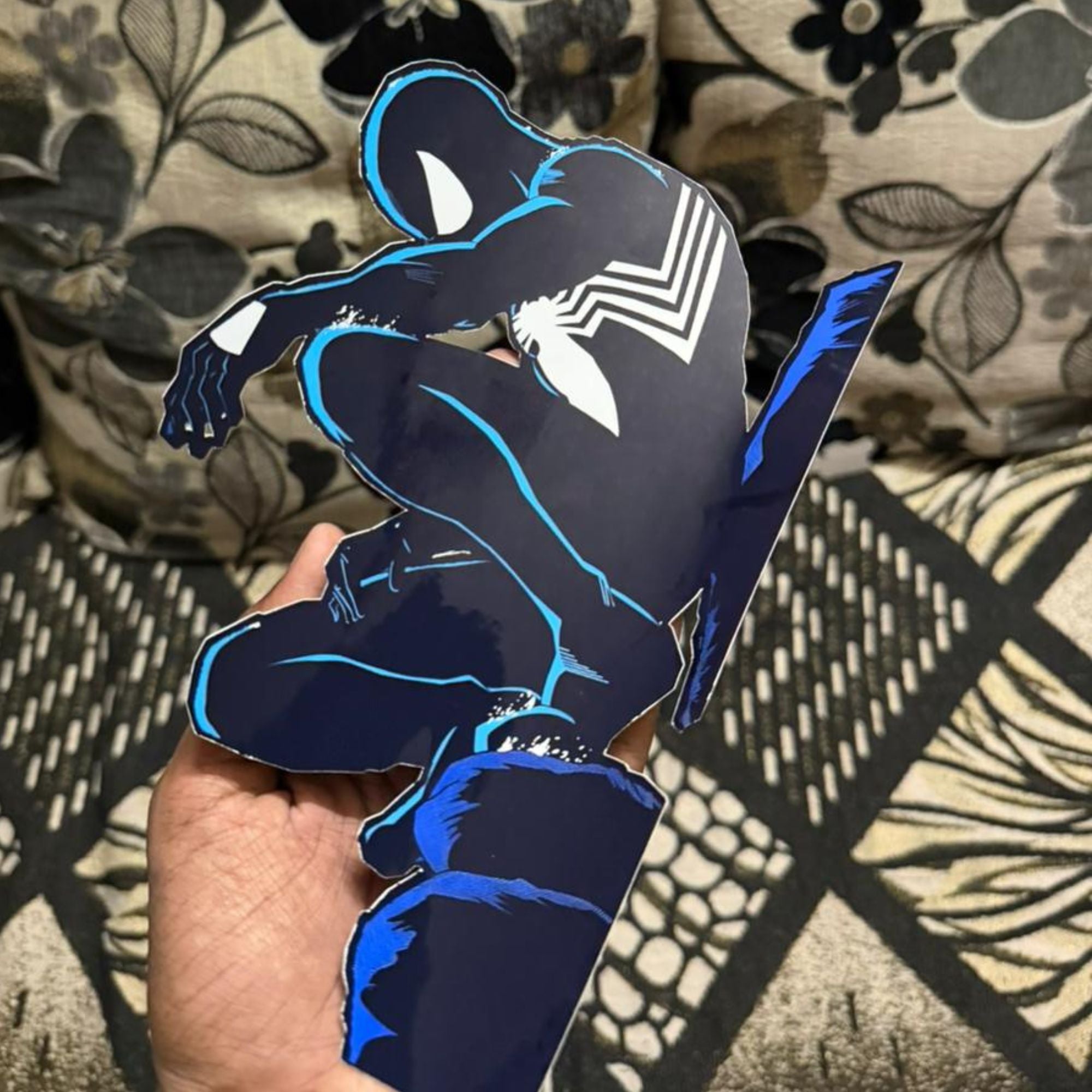 Hand holding a blue and black superhero cutout against a patterned fabric background